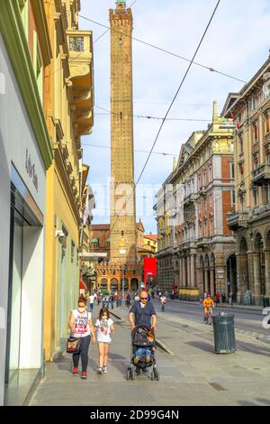 Bologna, Italien - 9. Mai 2020: Familien mit Kindern tragen die OP-Masken in der Via Rizzoli Straße mit zwei Türmen im Hintergrund. Phase 2 Stockfoto