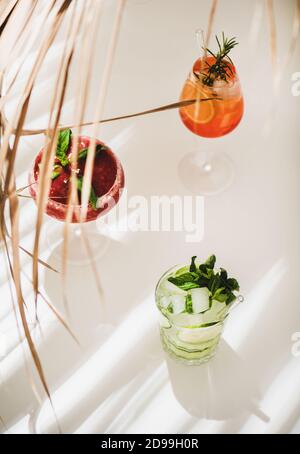 Beliebte Bar Sommer Eis alkoholische Cocktails. Gin-Tonic, Aperol Spritz und Erdbeerbasil Margarita in Gläsern auf weißem Hintergrund unter Strohdekor, selektiver Fokus Stockfoto