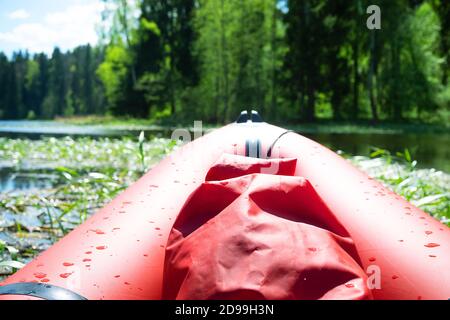 Wassersportangebote. Reisen Sie auf einem roten aufblasbaren Kajak auf dem kleinen Quellfluss, halten Sie unterwegs an und beobachten Sie die grünen Dickichte der Sumpfpflanzen Stockfoto