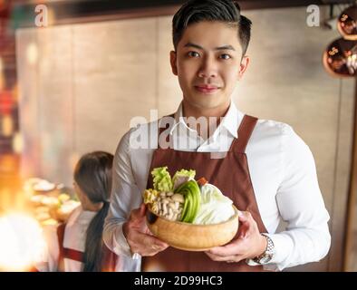 Der junge Kellner brachte Gemüse für den heißen Topf und servierte Gäste Im Restaurant Stockfoto