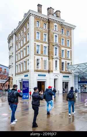 Touristen, die Gesichtsmasken tragen, machen Fotos auf ihren Handys vor dem Great Northern Hotel auf dem Vorplatz der King's Cross Station, London, Großbritannien Stockfoto