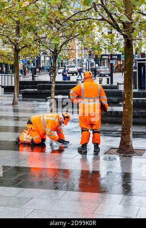 Zwei männliche Mitarbeiter von SGS in orangefarbener, gut sichtbarer Kleidung, die auf dem Vorplatz der King's Cross Station, London, Großbritannien, eine Inspektion durchführen Stockfoto