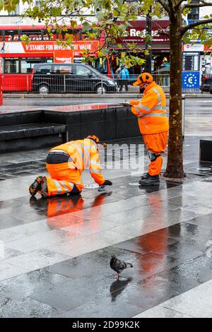 Zwei männliche Mitarbeiter von SGS in orangefarbener, gut sichtbarer Kleidung, die auf dem Vorplatz der King's Cross Station, London, Großbritannien, eine Inspektion durchführen Stockfoto