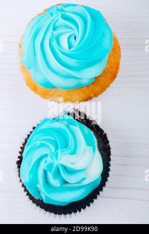 Zwei hausgemachte Muffins oder Cupcakes mit blauer Buttercreme Weißer Holzhintergrund Stockfoto