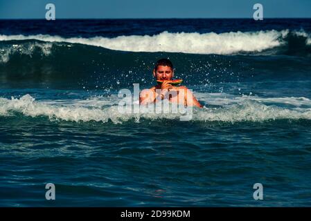 Kaukasischer Mann, der ein Stück Wassermelone im Meerwasser isst Selektiver Fokus Stockfoto