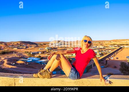 Touristenfrau, die beim Panoramablick auf die unterirdische Stadt Coober Pedy bei Sonnenuntergang und die umliegende Wüste vom Höhlenausblick aus sitzt. Südaustralisches Outback Stockfoto