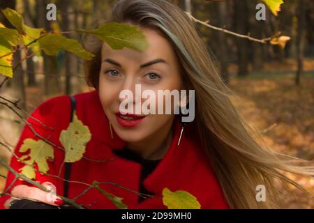 Blond im Herbst Park und Herbstblätter.Gelbe und rote Blätter. In einem roten Mantel Stockfoto