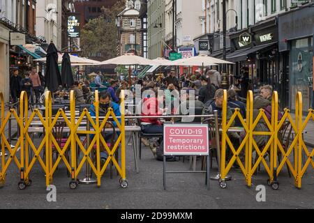 Leute, die draußen in Soho sitzen und Speisen und Getränke aus den verschiedenen Bars und Restaurants auf der Old Compton Street genießen. London Stockfoto