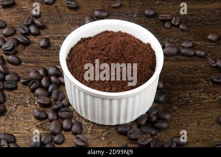 Geröstete Kaffeebohnen in Pulver in weißer Schüssel. Rustikaler Hintergrund Stockfoto