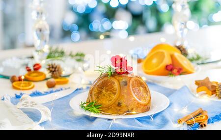 Traditioneller englischer Weihnachtspudding mit Orangen und Blumen in einem festlichen Rahmen mit Früchten, Gewürzen und Lichtern von Weihnachtsbaum dekoriert Stockfoto