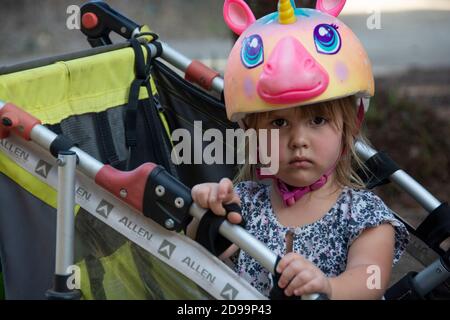 Ein kleines Mädchen mit einem Einhorn-Helm, der einen schlechten Tag im Park hat. Stockfoto