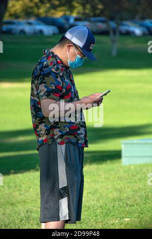 Ein asiatischer Mann mittleren Alters, der eine Maske trägt und sein Handy benutzt. Stockfoto