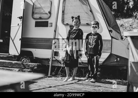 Graustufen Aufnahme von niedlichen Schwester und Bruder tragen Halloween-Kostüme Und gegen einen Camper stehen Stockfoto