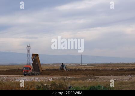 Planierraupen und LKWs arbeiten auf dem Feld bei bewölktem Wetter Stockfoto