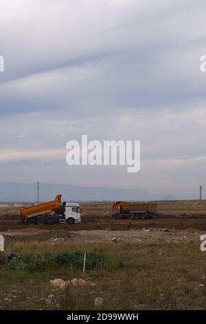 Planierraupen und LKWs arbeiten auf dem Feld bei bewölktem Wetter Stockfoto