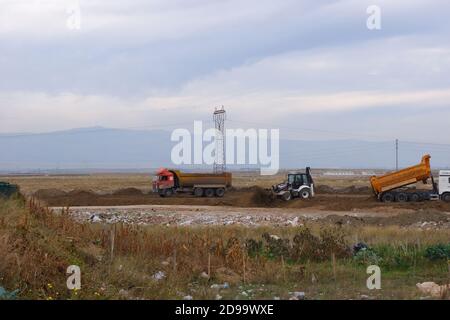 Planierraupen und LKWs arbeiten auf dem Feld bei bewölktem Wetter Stockfoto