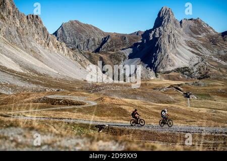 Zwei Männer fahren eBikes vorbei an der Schutzhütte Gardetta an der italienischen französischen Grenze im Maira-Tal, im Herbst in den Cottischen Alpen. Stockfoto