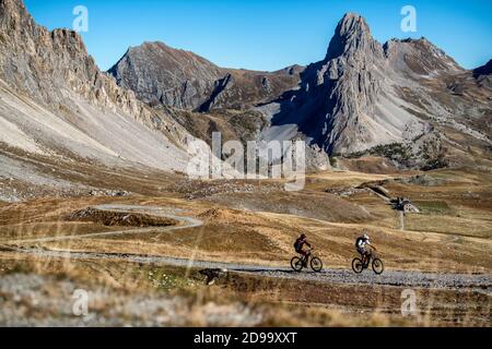 Zwei Männer fahren eBikes vorbei an der Schutzhütte Gardetta an der italienischen französischen Grenze im Maira-Tal, im Herbst in den Cottischen Alpen. Stockfoto