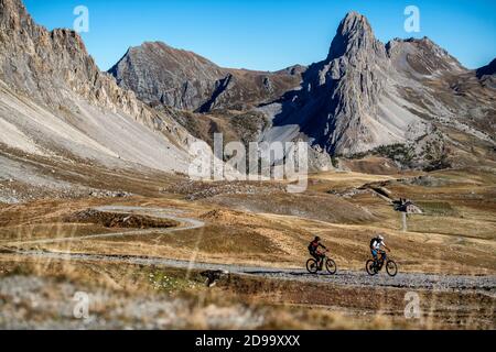 Zwei Männer fahren eBikes vorbei an der Schutzhütte Gardetta an der italienischen französischen Grenze im Maira-Tal, im Herbst in den Cottischen Alpen. Stockfoto