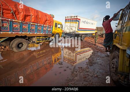 Chittagong, Bangladesch, Juli 2009 - Lastwagen warten auf eine verfallene Straße voller Wasser und Schlamm. Stockfoto