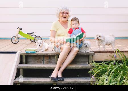 Großmutter liest Buch zu Enkel Junge auf der Veranda zu Hause Hinterhof. Bindung von Verwandten und Generationskommunikation. Alte Frau mit Baby Spaß haben Stockfoto
