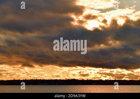 Forelle Lake, Michigan, USA. Die Wolken lassen die späte Nachmittagssonne kurz vor Sonnenuntergang erscheinen und projizieren eine Reflexion auf die Oberfläche des Sees. Stockfoto