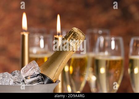 Selective focus of a champagne bottle neck in a champagne bucket with ice, with out of focus lit candles at the back. Alcohol and celebration concept. Stockfoto