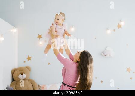 Eine Mutter und ein kleines Kind spielen im Kinderzimmer. Glückliche Familienbeziehungen. Mutter wirft eine glückliche einjährige Tochter auf. Stockfoto