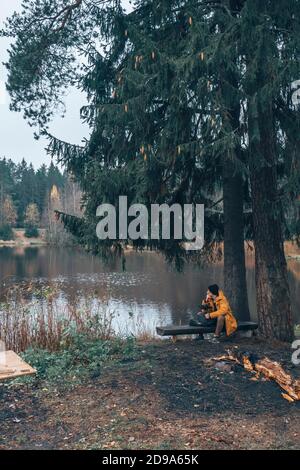 Ein Mann sitzt am See auf einer Bank. Neben einem Baum. Stockfoto