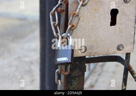 Ein neues braunes Vorhängeschloss mit einem glänzenden Bogen hängt an einer Kette an einer eisernen Tür. Stockfoto
