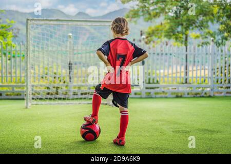 Kleine niedliche Junge in roten Fußball-Uniform Fußball spielen, Fußball auf dem Feld, im Freien. Aktives Kind macht Sport mit Kindern oder Vater, lächelnd glücklich Stockfoto