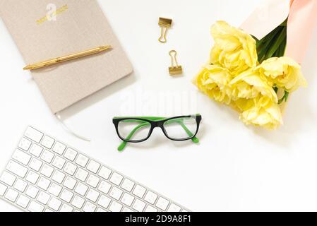 Trending minimalistischen flachen Lay eines Bloggers Arbeitsplatz. Notizblock, Stift, goldfarbene Büroklammern und ein Bündel gelber Tulpen, Brille, Tastatur auf einem W Stockfoto