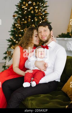 Die Familie genießt die Feiertage und feiert gemeinsam ihr erstes Weihnachtsfest. Glückliche Familie im Zimmer mit dem Weihnachtsbaum. Stockfoto