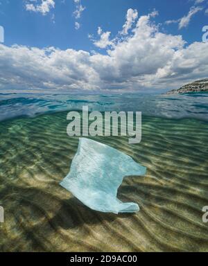 Plastikmüll Verschmutzung im Ozean, eine Plastiktüte unter Wasser und wolkig blauer Himmel, Split-Ansicht über und unter Wasseroberfläche Stockfoto