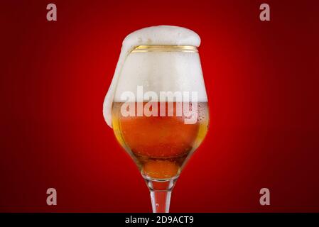 Glas Bier mit Schaumstoffkappe isoliert auf rotem Hintergrund, Stockfoto
