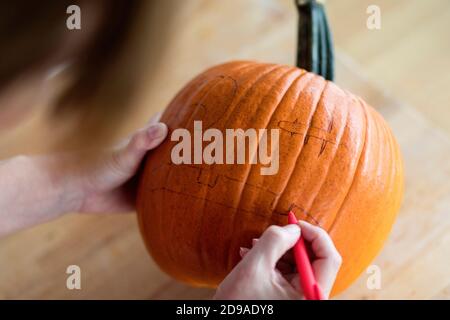 Eine Frau in der Küche malt einen Kürbis für Halloween in einem Zimmer Stockfoto