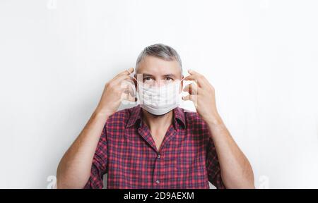 Ein Mann in einem rot karierten Hemd trägt einen Arzt Maske gegen eine weiße Wand Stockfoto