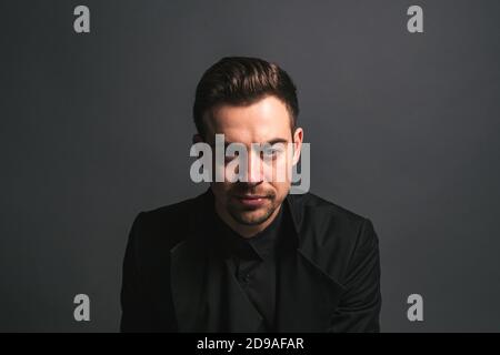 Studioportrait eines jungen Kaukasiers in schwarzer Jacke, ernsthaft auf die Kamera schauend, vor schlichtem Studiohintergrund Stockfoto