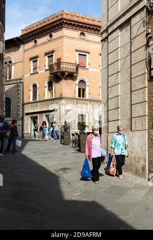 Zwei ältere Frauen, die Gesichtsmasken tragen und Einkaufstaschen tragen, wandern entlang einer Straße in Siena, Toskana, Italien Stockfoto