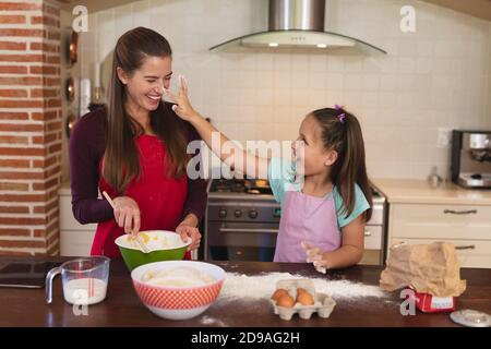 Kaukasische Frau mit ihrer Tochter Backen in einer Küche und Schürze tragen Stockfoto