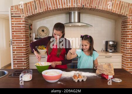 Kaukasische Frau mit ihrer Tochter Backen in einer Küche und Schürze tragen Stockfoto