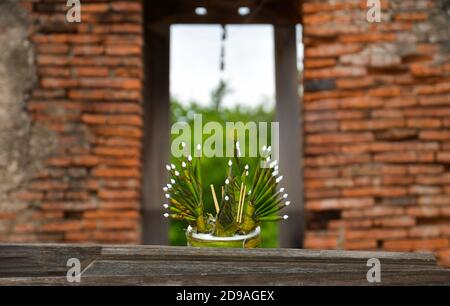 Ein krathong in einem alten Holzfenster eines buddhistischen Backsteintempels. Die Krathongs bestehen aus Blumen, Kerzen, Bananenblättern und Räucherstäbchen und sind gi Stockfoto