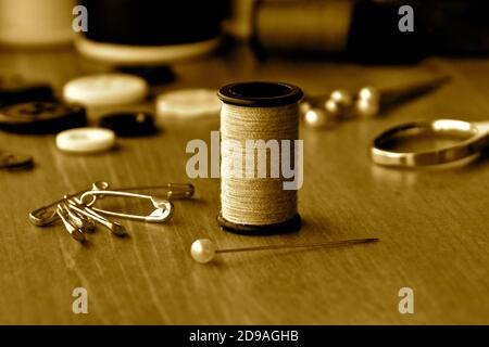 Eine Nahaufnahme einer Baumwollrolle unter einer Reihe von Nähzubehör in Sepia-Tönen. Stockfoto