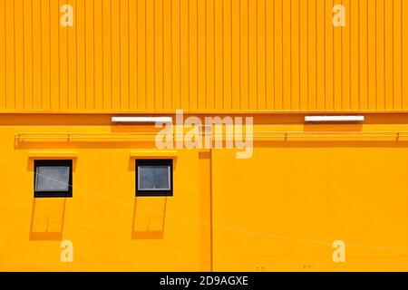 Ein hellgelbes Gebäude aus Stein und Wellblech mit 2 Fenstern mit Schatten gebaut. Stockfoto