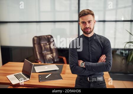 Moderner Geschäftsmann, der im Büro mit gekreuzten Armen steht Stockfoto