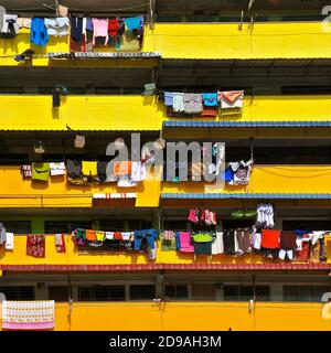 Bunte Wäsche zum Trocknen auf den gelben Balkonen eines Wohnblocks mit hoher Dichte in Asien. Stockfoto