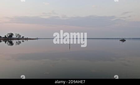 Minimalistisches Wasserbild mit ruhigen Gewässern, reflektierenden Bildern der Silhouetten von Bäumen und einem rustikalen hölzernen Angelponton. Stockfoto