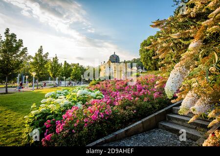 Marianske Lazne / Tschechische Republik - 8. August 2020: Blick auf die Kolonnade von Maxim Gorki und den singenden Springbrunnen über rosa und weißen Blumen. Sommertag. Stockfoto