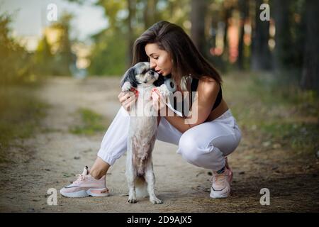 Eine junge Frau mit ihrem süßen Shih Tzu sitzt auf einem Pfad im Wald. Stockfoto