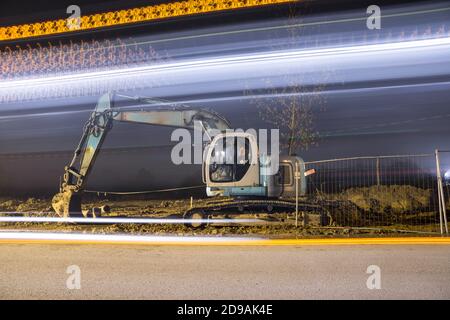 Blauer Bagger arbeitet nachts auf der Straße Stockfoto